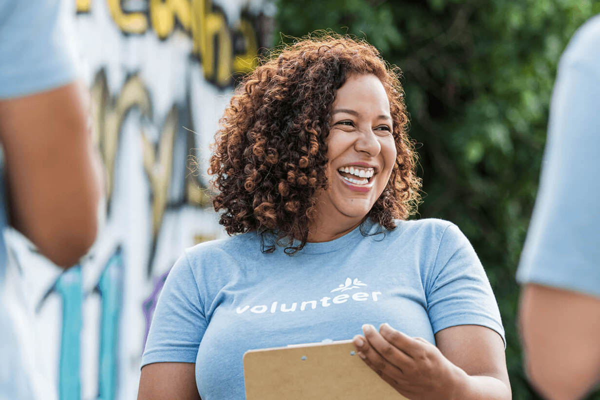 A young woman holding a meeting with volunteers holding a clipboard and wearing a tshirt with the word volunteer on the front 